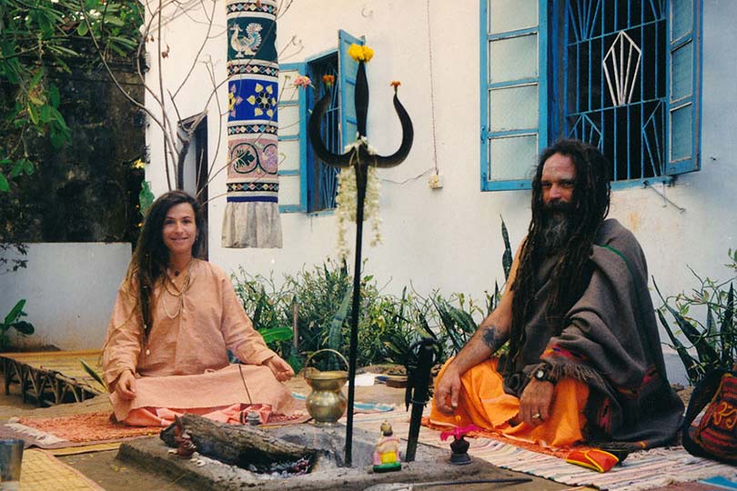 Goa Gil and Ariane siting in front of outdoor fireplace with shiva trident